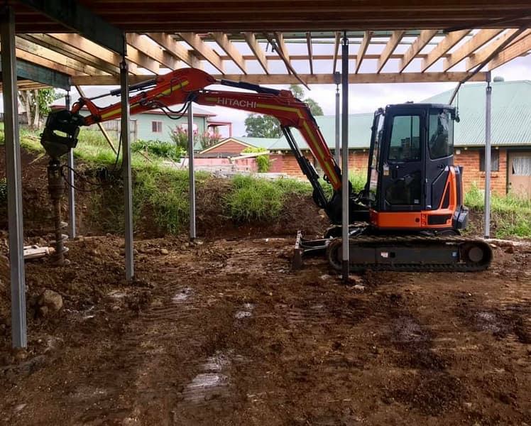 Hitachi excavator completing detailed work beneath a raised home